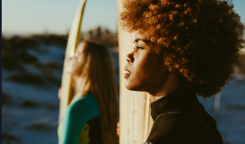 Close Up Of Young Woman Holding A Surfboard And Looking At The Sunset With Her Friend Photo